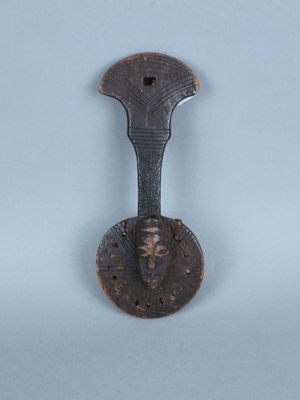 une cuillère en métal sur laquelle est représenté un visage, posée sur une surface blanche