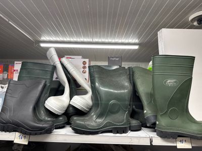 Plusieurs paires de bottes en caoutchouc sont posées sur une étagère dans un magasin.