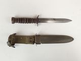 pair of military knifes on a white surface with a leather sheath