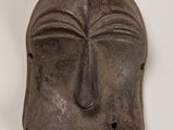un masque métallique sur lequel est représenté un visage, posé sur un fond blanc