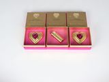 three boxes of gold and pink heart shaped brooches on a white surface