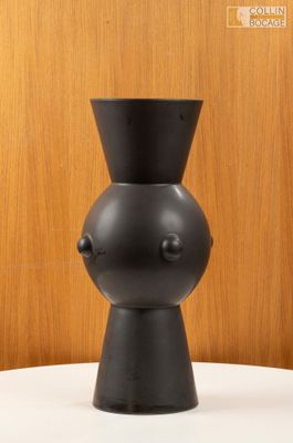 un vase noir posé sur une table, avec un mur en bois en arrière-plan