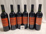 six bottles of red wine are lined up on a table