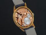 a gold watch with a black leather strap on a black surface