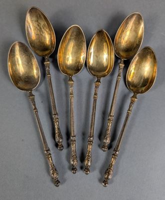 six antique spoons are lined up in a row on a gray surface