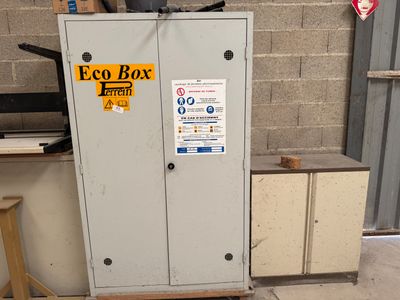 une armoire métallique sur laquelle est apposée une pancarte, devant un bâtiment