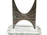 une sculpture en métal posée sur un socle transparent, sur fond blanc