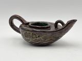 a brown teapot with a green handle on a white surface