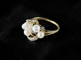 a gold ring with pearls and diamonds on a black background