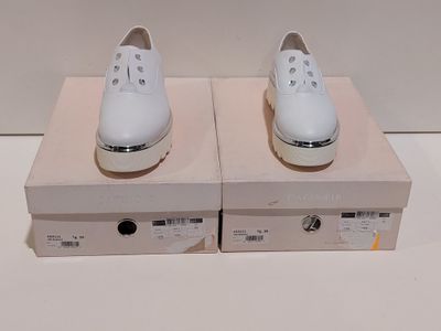 une paire de chaussures blanches posée sur une boîte, elle-même posée sur une surface blanche