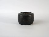 un vieux vase en bois noir posé sur une surface blanche