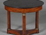une table ronde avec un plateau en marbre noir reposant sur un piètement en bois