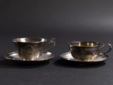 deux tasses et soucoupes en argent posées sur un fond noir