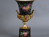 un vase décoré de fleurs, posé sur un socle, sur fond gris