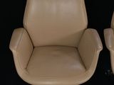 pair of tan leather office chairs on casteors against a black background