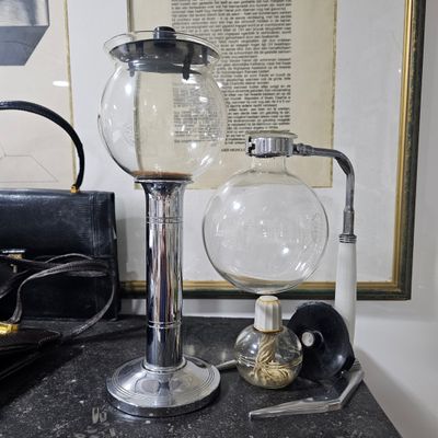 a glass coffee pot on a table next to a pair of glasses and a pair of scissors