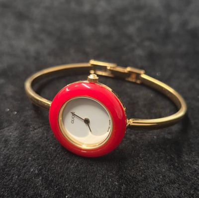 une image représentant une montre-bracelet rouge et dorée posée sur une surface noire
