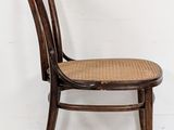 an image of a wooden chair with wicker seat against a white wall