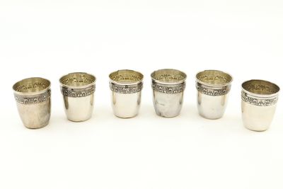 six verres à shot en argent alignés en rangée sur une surface blanche