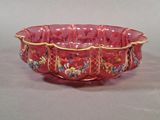a red glass bowl with gold trimmings and flowers on it