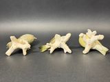 three small figurines of birds on a branch with leaves