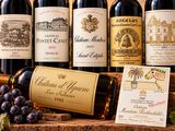 plusieurs bouteilles de vin posées sur une table en bois, à côté d'une grappe de raisin
