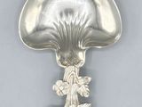 an antique silver spoon with a mushroom shaped handle on a gray surface