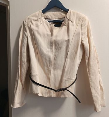 une veste beige avec une ceinture noire, suspendue à un cintre accroché au mur près de la porte
