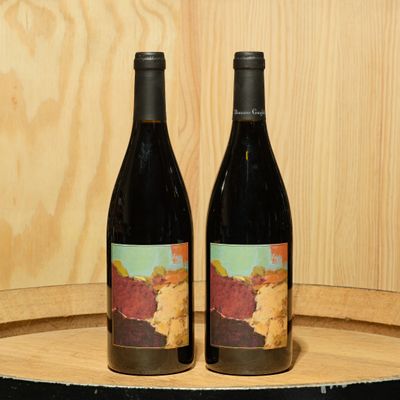 two bottles of wine sitting on top of a wooden barrel