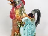 un coq en céramique qui tient une pancarte dans son bec