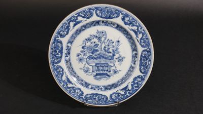 une vieille assiette bleue et blanche sur laquelle est représenté un panier de fleurs