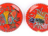 two red plates with colorful designs on them on a white surface