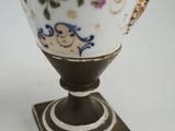 a white vase with a gold handle on a stand