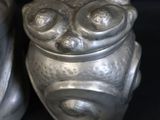 two silver vases with faces on them on a black background