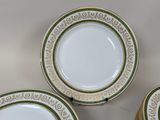 three white and green plates with gold rims on a white surface