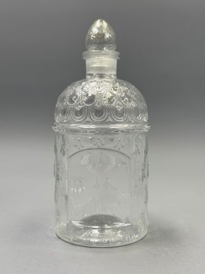 une bouteille en verre transparent avec un bouchon argenté, posée sur une surface grise