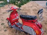 un scooter rouge avec une selle à carreaux, garé près d'un arbre