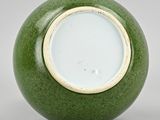 a green vase sitting on top of a table next to a white wall