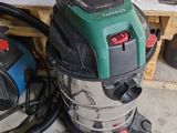 a green and black vacuum sitting on the floor next to a pile of wood