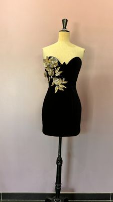 une robe noire posée sur un mannequin, devant un mur rose