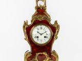 une horloge rouge et dorée posée sur une surface blanche