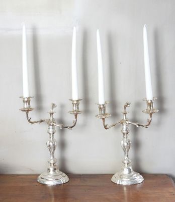 trois chandeliers en argent avec des bougies blanches posés sur une table en bois