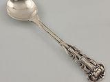 une cuillère en argent ornée d'un motif décoratif, posée sur une surface blanche