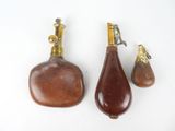 trois flacons de parfum anciens en laiton et en bois posés sur une surface blanche