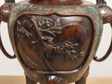 a bronze vase on a wooden stand with a handle