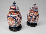 une paire de vases chinois avec couvercles, posés sur des socles, sur une surface grise