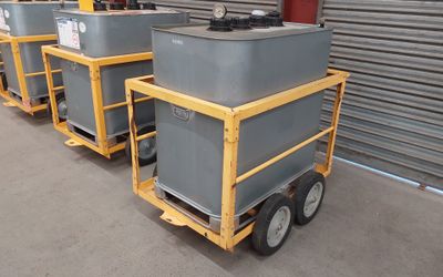 quatre conteneurs gris posés sur un chariot devant un immeuble