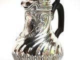 a silver pitcher with a black handle on a white surface