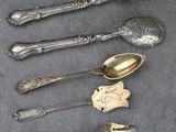 cinq cuillères en argent et une fourchette sont alignées sur une table