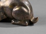 bronze statue of a rabbit sitting on its hind legs on a gray surface